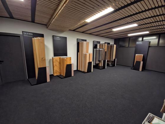 Espositori verticali con campioni di pavimenti in legno, pavimento in moquette scura e soffitto a doghe di legno